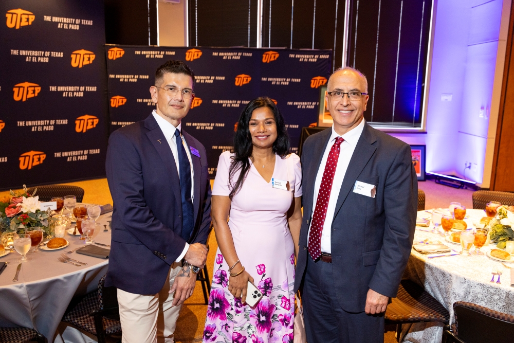 Three attendees pose together in front of a UTEP backdrop at a formal reception.